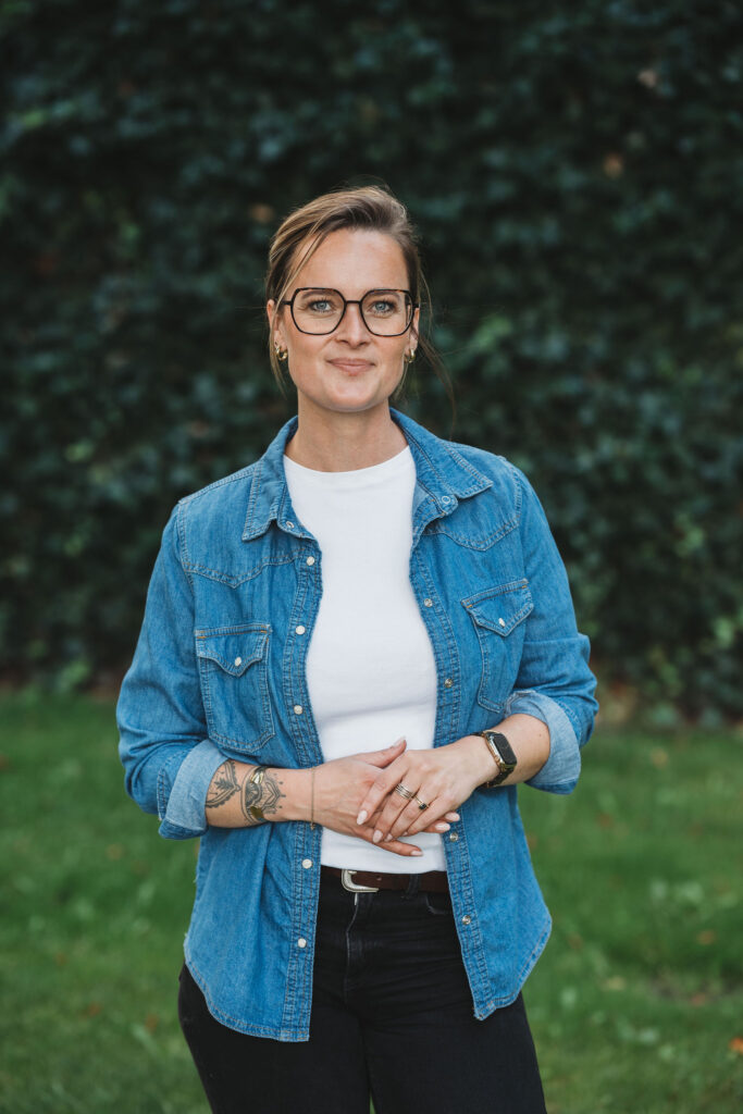 Rebekka Hviid smiler og poserer foran en grøn hæk.